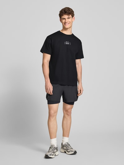 Männermodel trägt T-Shirt mit Label-Print von HALO in Schwarz, reine Baumwolle, Regular Fit, Rundhalsausschnitt, Ganzkörperansicht von vorne.