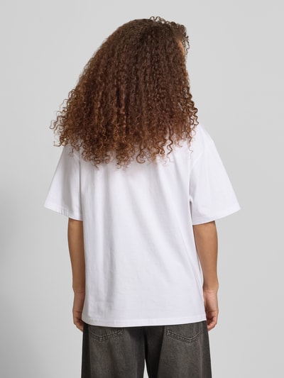 Frauenmodel trägt T-Shirt mit rückseitigem Motiv-Print von REVIEW aus reiner Baumwolle, Oversized mit Rundhalsausschnitt, Rückenlänge 68 cm, Ganzkörperansicht Rückansicht.