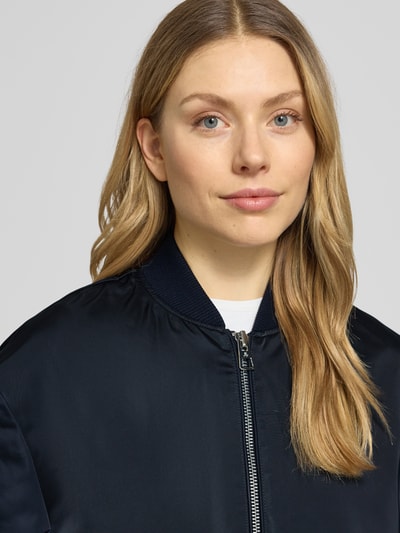 Kobieta prezentuje Regular Fit Blouson-Mantel mit College-Kragen od Marc O'Polo, efekt: jednolity kolor, satyna, naszywka z logo, zamek błyskawiczny dwustronny, długi rękaw, wpuszczane kieszenie, kieszeń wewnętrzna, krój regular fit, kształt kołnierza: kołnierz college, kolor granatowy. Zbliżenie na górną część ciała.