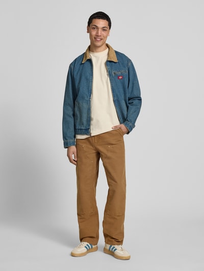 Männermodel trägt Jeansjacke mit Label-Detail und Reißverschluss von Dickies in Blau, Reine Baumwolle, Regular-Fit, Umlegekragen, Eingrifftaschen, Ganzkörperansicht von vorne.
