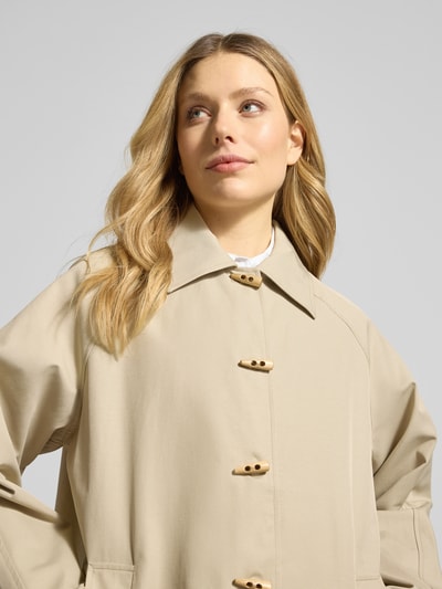 Frauenmodel trägt Mantel mit Umlegekragen und Eingrifftaschen Modell 'GEZAV' von ICHI aus Baumwoll-Mix in Beige, Relaxed-Fit, Nahaufnahme Oberkörper. Rückenlänge 98 cm, Schulterbreite 41 cm, Brustweite 58 cm, Ärmellänge 47 cm bei Größe 36.