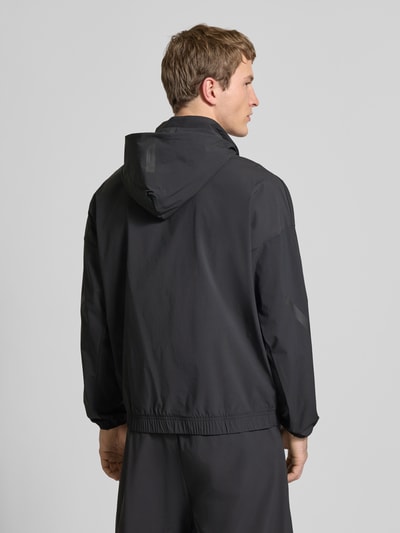 Männermodel trägt Regular Fit Jacke mit Kapuze von adidas Sportswear in Schwarz, Elastischer-Material-Mix, Logo-Print, Ganzkörperansicht Rückansicht.