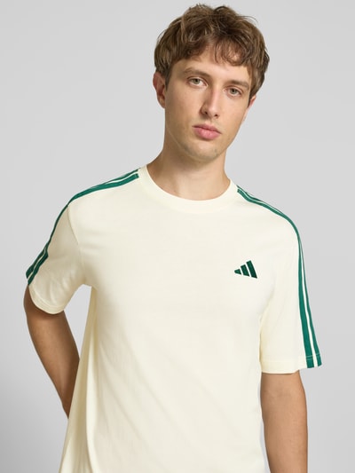 Männermodel trägt Regular Fit T-Shirt aus reiner Baumwolle Modell 'M 3S SJ LC T' von adidas, cremefarben mit grünen Streifen, Herren T-Shirt von adidas Sportswear, Nahaufnahme Oberkörper.