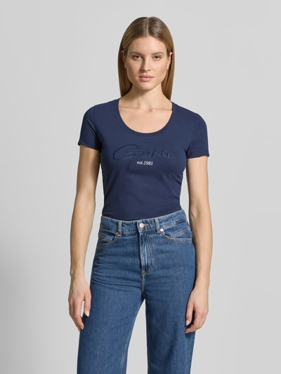 Vrouwenmodel draagt T-shirt met U-hals model 'SCRIPT' van Guess, mix van katoen en elastaan, nauwsluitend model, labelstitching, ruglengte bij maat S 61 cm, donkerblauw, vooraanzicht bovenlichaam