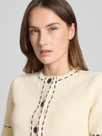 Kobiece modelka nosi Slim Fit Strickjacke mit aufgesetzten Taschen od Rich & Royal, bawełniana mieszanka, krój slim fit, beżowy kolor, teksturowany materiał, naszywane kieszenie, półrękaw, okrągły dekolt, guziki na całej długości, elastyczne wykończenia, widoczne ciemne przeszycia, kontekst: długość pleców w rozmiarze S: 42 cm, długość rękawa w rozmiarze S: 26 cm, zbliżenie na górną część ciała