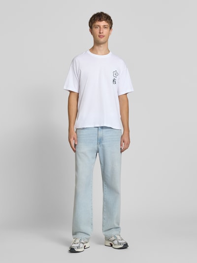 Männermodel trägt Relaxed Fit T-Shirt aus reiner Baumwolle Modell "DYLAN" von JACK & JONES, Print-Detail, weiße Farbe, Ganzkörperansicht von vorne.