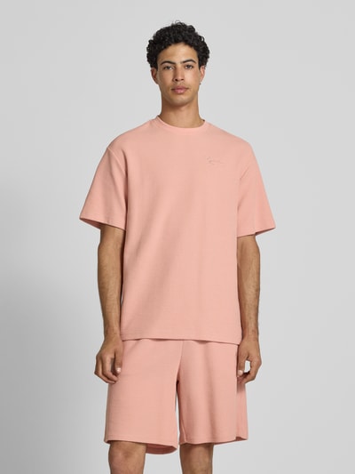 Männermodel trägt Oversized Fit T-Shirt mit Strukturmuster von KARL KANI in Rosa, aus Baumwoll-Mix mit Logo-Stitching, Ganzkörperansicht von vorne.