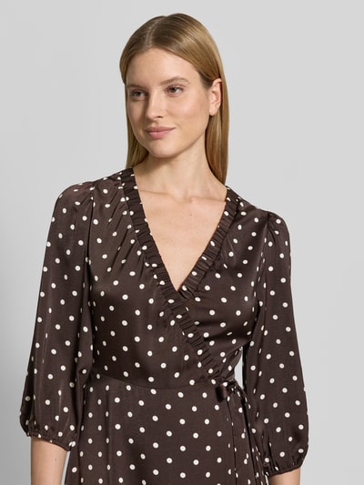 Frauenmodel trägt Regular Fit Maxikleid mit V-Ausschnitt von Neo Noir aus braunem Satin mit weißen Punkten, 3/4-Arm, Wickel-Optik, Nahaufnahme Oberkörper.