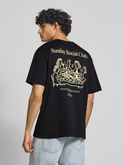 Männermodel trägt Relaxed Fit T-Shirt aus reiner Baumwolle Modell 'FRED DU MARTIN' von Only & Sons in Schwarz mit Motiv-Print, Ganzkörperansicht Rückansicht.