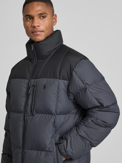 Męski model nosi Regular Fit Daunenjacke mit Zweiwege-Reißverschluss Modell 'GORHAM' od Polo Ralph Lauren, dwukolorowa, pikowana kurtka z logo, kieszenie na zamek, stojący kołnierz, elastyczne mankiety, widok na górną część ciała z przodu.