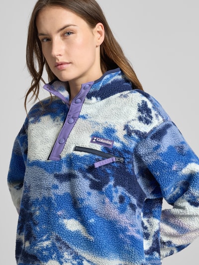 Frauenmodel trägt Regular Fit Pullover mit Logo-Patch Modell 'Helvetia' von Columbia, Fleece-Optik in Blau-Weiß, Brusttasche, Knopfleiste, Nahaufnahme Oberkörper.