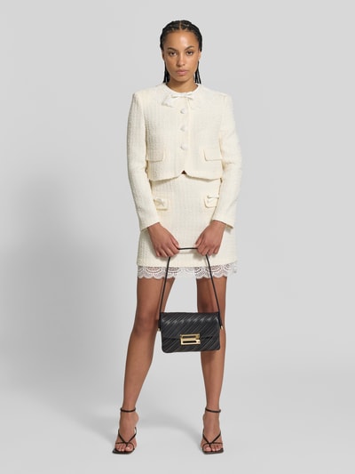 Frauenmodel trägt Henkeltasche mit glatter Lederoptik und Metallverschluss von Victoria Beckham, unifarben, glänzend, Logo-Prägung, Ganzkörperansicht von vorne.