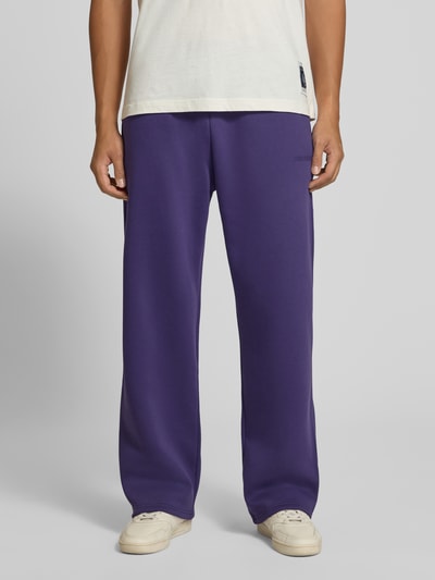 Männermodel trägt Straight Fit Sweatpants aus Baumwoll-Mix mit Label-Detail von REVIEW in Lila, mit Eingrifftaschen, Ganzkörperansicht von vorne.
