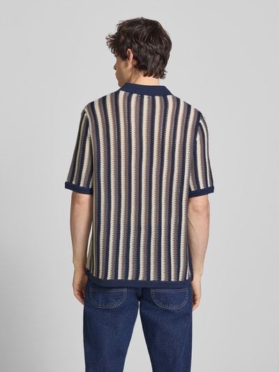 Männermodel trägt Regular Fit Poloshirt aus Baumwoll-Mix Modell 'THUE' von Only & Sons, Optik:Allover-Muster, Gestreift, Lochstrickmuster, Struktur, Polokragen, V-Ausschnitt, Ärmelform: Kurzarm, Ärmelabschluss: Gerippt, Rumpfabschluss: Gerippt, Farben beige und dunkelblau, Ganzkörperansicht Rückansicht.