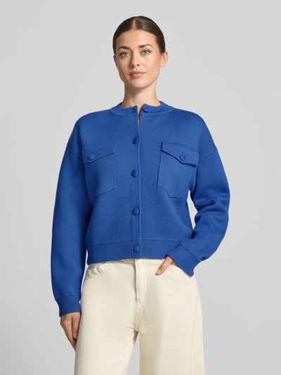 Frauenmodel trägt Strickjacke mit Brusttaschen von Rich & Royal in Blau, lockere Passform, gerippte Abschlüsse, Nahaufnahme Oberkörper.