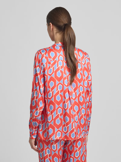 Vrouwenmodel draagt Slim Fit Hemdbluse aus reiner Viskose van Milano Italy met rood, blauw en wit geometrisch patroon, ruglengte maat 36: 65 cm, mouwlengte maat 36: 62 cm, doorlopende knoopsluiting, overhemdkraag, blouse met lange mouwen, ganzlichamige achteraanzicht.