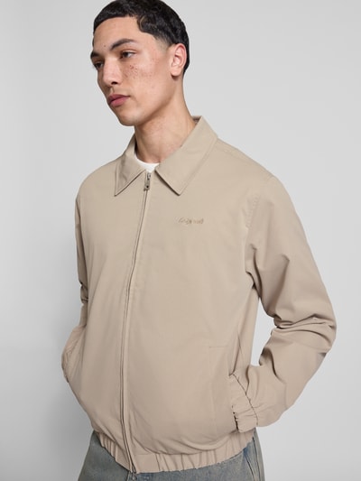 Männermodel trägt Jacke mit Zweiwege-Reißverschluss Modell 'CATSKILLS' von Jack & Jones in Beige, Umlegekragen, Label-Stitching, Nahaufnahme Oberkörper.