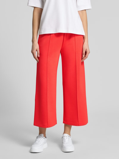 Frauenmodel trägt Culotte mit elastischem Bund von Christian Berg Woman im leuchtend roten Material-Mix mit Längsnähten und Wide-Leg-Pants, Nahaufnahme Oberkörper bis Knöchel.
