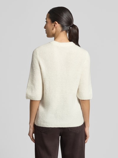 Kobiece modelka ma na sobie Strickjacke mit Woll-Anteil Modell 'Jinie Hope' od MSCH Copenhagen, kremowy materiał, prosty krój, widok całej sylwetki od tyłu.