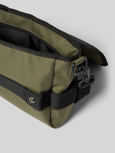 Produktfoto, grüne Tasche mit Logo-Patch von Carhartt Work In Progress, wasserabweisendes Material, Überschlag, schwarzer Schulterriemen, Detailaufnahme
