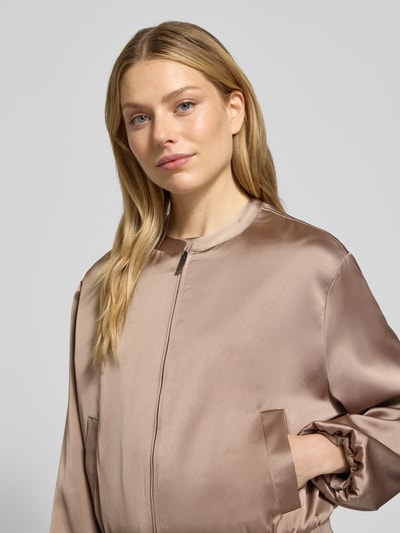 Frauenmodel trägt Blouson mit Reißverschluss Modell 'Jupita' von OPUS in Beige, glatte Oberfläche, seitliche Taschen, Nahaufnahme Oberkörper.