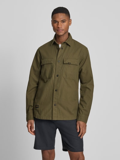 Männermodel trägt Regular Fit Hemdjacke aus reiner Baumwolle von camel active in Olivgrün mit Umlegekragen, durchgehende Knopfleiste, Langärmelig, Brusttaschen, Statement-Patch, Label-Detail, Rückenlänge 74 cm, Schulterbreite 44 cm, Brustweite 53 cm, Ärmellänge 66 cm; Ganzkörperansicht von vorne.