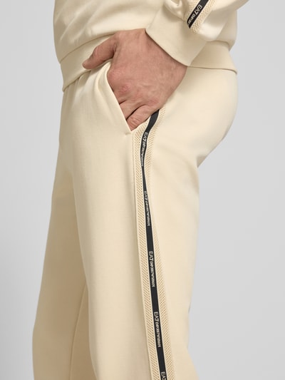 Männermodel trägt Sweatpants aus Baumwoll-Mix von EA7 Emporio Armani in Beige mit Eingrifftaschen, lockerem Schnitt, Nahaufnahme Oberschenkel.