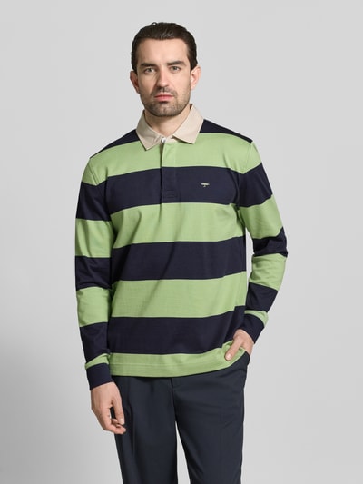 Männermodel trägt Regular Fit Poloshirt mit Streifenmuster und Label-Stitching von Fynch-Hatton, Farbkontraste grün und navy, reine Baumwolle, Knopfverschluss, Polokragen, Longsleeve, Ganzkörperansicht von vorne.