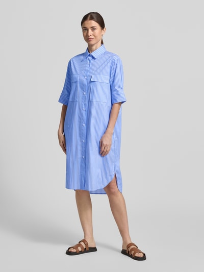 Modelka nosi sukienkę koszulową Relaxed Fit Hemdblusenkleid mit Brusttaschen Modell 'Daliya' od JOOP! z elastycznej mieszanki bawełny, nadruk z logo na całej powierzchni, półrękaw, kołnierzyk koszulowy, listwa guzikowa na całej długości, niebieskie i białe paski, kieszenie na piersi; długość tyłu w rozmiarze 36: 108 cm, szerokość w rozmiarze 36: 52 cm, długość rękawa w rozmiarze 36: 30 cm. Całopostaciowy widok z przodu.