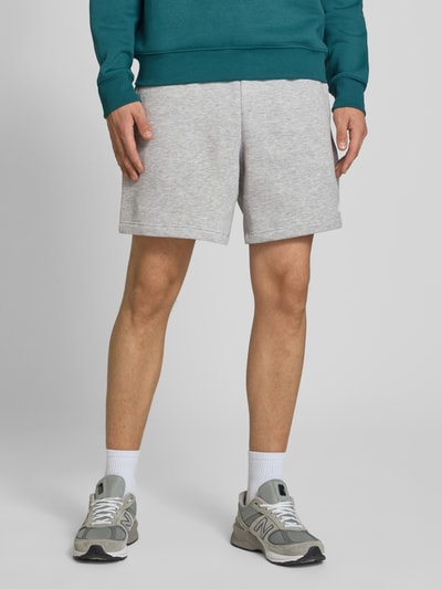 Männermodel trägt Relaxed Fit Shorts mit Logo-Stitching von New Balance in Hellgrau, Baumwoll-Mix, elastischer Bund, Ganzkörperansicht von vorne.