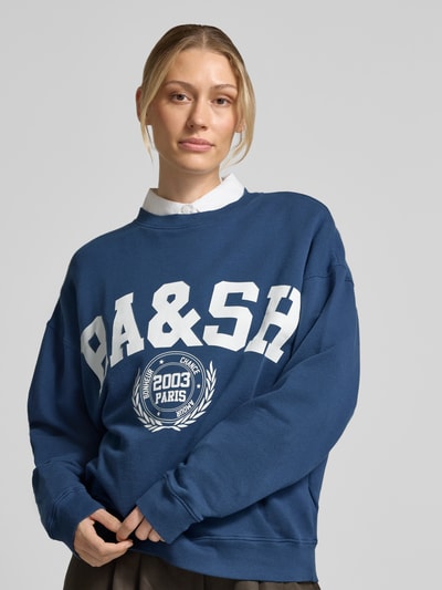 Modelka kobieca ma na sobie bluzę Sweatshirt mit Label-Print Modell 'BENJAMIN' od ba&sh, kolor ciemnoniebieski, mieszanka bawełny i elastanu, luźny krój, okrągły dekolt, nadruk z logo z przodu, długie rękawy, tekstura miękka, przód gładki, widoczne przeszycia, całkowity widok klatki piersiowej, zdjęcie z przodu.