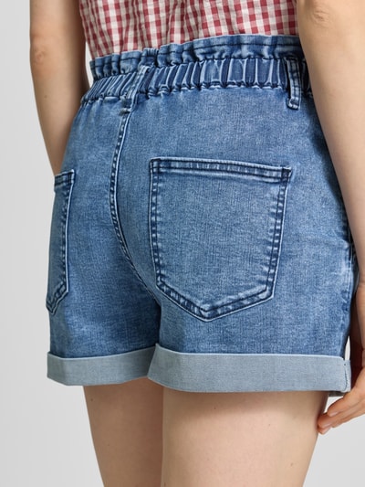 Frauenmodel trägt Straight Fit Shorts in Denim-Optik mit Viskose-Anteil von Apricot, strukturierte blaue Baumwollmischung, Elastikbund, Rückansicht Detailaufnahme.