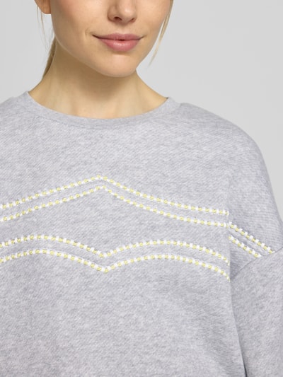 Frauenmodel trägt Oversized Sweatshirt mit Rundhalsausschnitt von Lanius aus Baumwoll-Material-Mix in Hellgrau mit Label-Stitching, Nahaufnahme Oberkörper.