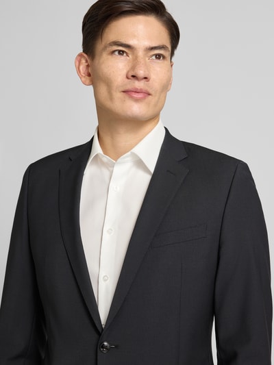 Męski model nosi Regular Fit 2-Knopf-Sakko mit Woll-Anteil od Strellson, mieszanka materiałów z dodatkiem wełny, klapy otwarte, listwa z 2 guzikami, brustasza, kieszenie z patką, długość tyłu 72 cm, szerokość ramion 45 cm, długość rękawów 62 cm, kolor ciemny, gładka faktura. Nahaufnahme górnej części ciała.