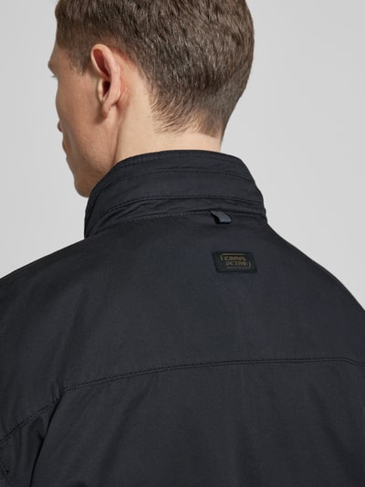 Męski model nosi Jacke aus reiner Baumwolle mit Brusttaschen od camel active, czarny kolor, gładka tekstura, widok od tyłu, zbliżenie na ramiona. Prosty krój, stójka z ochroną podbródka, długość tyłu w rozmiarze 50: 73 cm, szerokość ramion w rozmiarze 50: 52 cm, szerokość w rozmiarze 50: 58 cm, długość rękawa w rozmiarze 50: 64 cm.