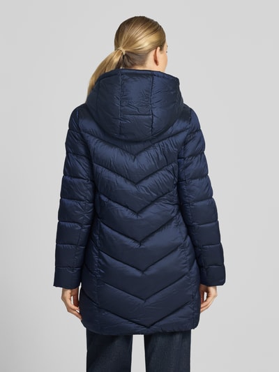 Frauenmodel trägt Steppmantel mit Kapuze und Reißverschlusstaschen von MICHAEL Michael Kors in Dunkelblau, glatte Struktur, Ganzkörperansicht Rückansicht. Gerader Schnitt, Rückenlänge 86 cm, Schulterbreite 43 cm, Brustweite 50 cm, Ärmellänge 62 cm, Kapuze mit Tunnelzug und Kordelstopper, Stehkragen, seitliche Reißverschlusstaschen.
