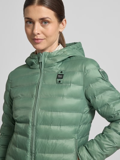 Frauenmodel trägt Steppjacke mit Zweiwege-Reißverschluss Modell 'ELLIS' von Blauer Usa in Grün, Kapuze, Slim Fit, Nahaufnahme Oberkörper, Rückenlänge bei Größe S 57 cm, Schulterbreite 35 cm, Brustweite 48 cm, Ärmellänge 60 cm.