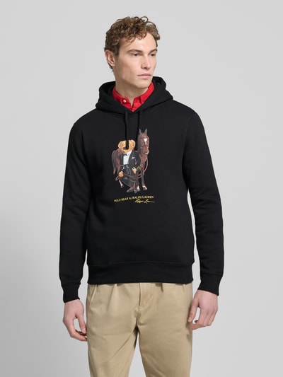 Mannermodel draagt Hoodie met Labelprint van Polo Ralph Lauren in zwart, katoenmix, los model, capuchon met tunnelkoord, ribboorden, Ganzkörperansicht von voren. Ruglengte maat M: 67 cm, mouwlengte maat M: 65 cm.