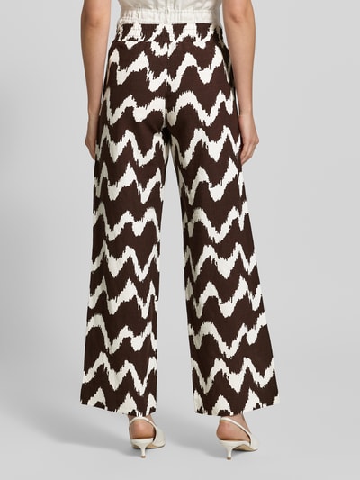 Kobieta prezentuje spodnie z szerokimi nogawkami Wide Leg Pants aus Viskose-Mix mit elastischem Bund od OPUS PANTS, mieszanka wiskozy z lnem, krój loose fit, model 'Malotta', elastyczny pas, szerokość w rozmiarze 36: 37 cm, długość wewnętrzna nogawki w rozmiarze 36: 79 cm, wzór zygzakowaty w brązie i bieli, wyrazista tekstura, widok całej sylwetki z tyłu.