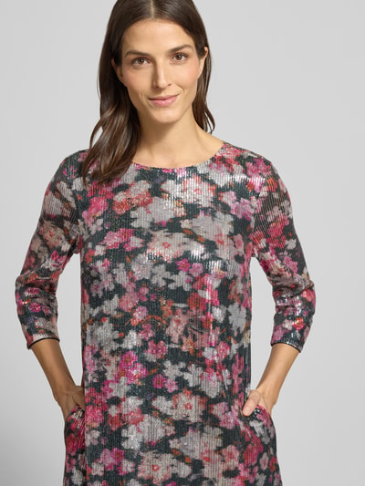 Kobiece modelka nosi Knielanges Kleid mit Allover-Muster und Paillettenbesatz von Christian Berg Woman, kwiatowy wzór na całej powierzchni, prosty krój, długość do kolan, okrągły dekolt, rękaw o dł. 3/4, cekinowe obszycie, czysta wiskoza, szerokość w rozmiarze 36: 48 cm, długość tyłu w rozmiarze 36: 96 cm, długość rękawa 47 cm, widok na górną część ciała od przodu.
