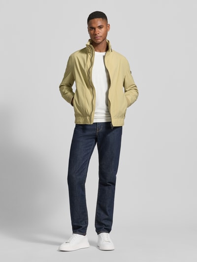 Männermodel trägt Regular Fit Jacke mit Stehkragen von bugatti in Beige mit Zweiwege-Reißverschluss, Ganzkörperansicht von vorne.