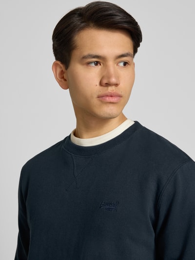 Männermodel trägt Sweatshirt mit Rundhalsausschnitt und Label-Stitching von Superdry aus katoenmix, regular fit, nahaufnahme oberkörper.