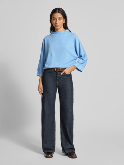 Frauenmodel trägt Longsleeve mit 3/4-Ärmel Modell 'Sagida' von Opus in Hellblau, Material-Mix mit Viskose-Anteil, Lockerer-Schnitt, Stehkragen, gerippte Abschlüsse, Rückenlänge 60 cm bei Größe 36, glatte Textur, Ganzkörperansicht von vorne.