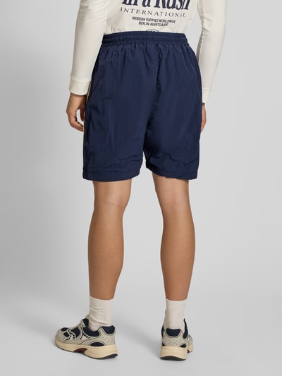 Männermodel trägt Shorts mit Label-Stitching Modell 'Slipstream' von PROHIBITED in Dunkelblau, lockere Passform, Rückansicht Ganzkörperansicht.