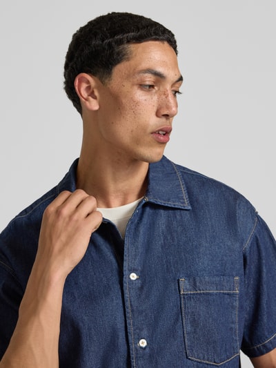 Männermodel trägt Modern Fit Jeanshemd mit Brusttasche Modell 'AUSTIN' von Jack & Jones aus reiner gewachster Baumwolle, Nahaufnahme Oberkörper.