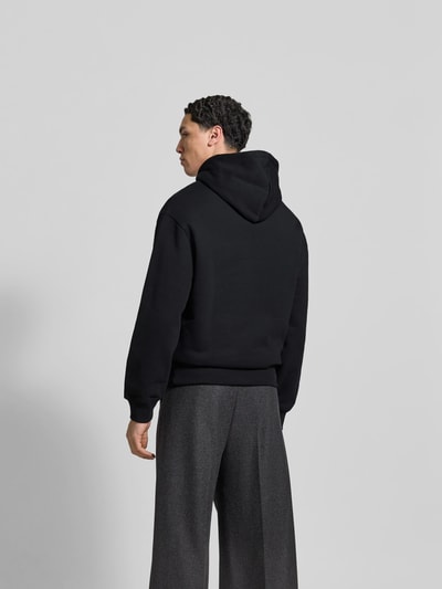 Männermodel trägt Hoodie mit Label-Stitching von MAISON KITSUNÉ in Schwarz, lockere Passform, Ganzkörperansicht Rückansicht.