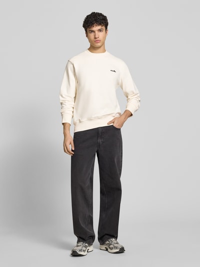 Męski model nosi Sweatshirt mit Rundhalsausschnitt und Label-Stitching von Ellesse, kremowy, bawełniany, krój regular fit, długość tyłu 66 cm, długość rękawa 64 cm, widok całej sylwetki z przodu.