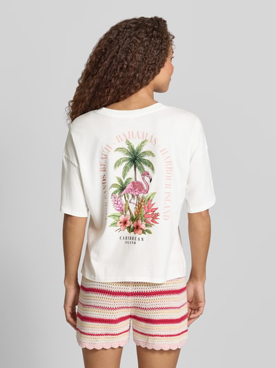 Frauenmodel trägt Damen T-Shirt von Only, Modell 'Boxy Fit T-Shirt aus reiner Baumwolle Modell 'LUCY'' mit Optik: Unifarben, Boxy-Fit Passform, Motiv-Print Applikation und Rückenprint, Rundhals, Kurzarm, Material: Reine Baumwolle, in Weiß mit buntem Print, Struktur glatt, Ganzkörperansicht Rückansicht.