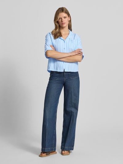 Frauenmodel trägt Regular Fit Hemdbluse aus reiner Baumwolle Modell 'THYRA' von Only mit hellblau-weißem Allover-Muster, Reverskragen und kurzen Ärmeln, Ganzkörperansicht von vorne.