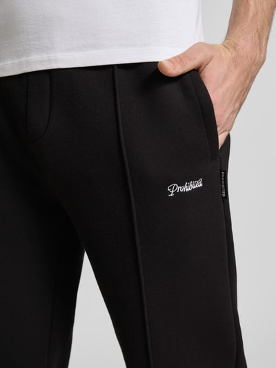 Mannelijk model draagt Loose Fit Sweatpants mit Label-Stitching und elastischem Bund van PROHIBITED in zwart, katoenmix, detailopname zijkant, binnenbeenlengte maat M 80 cm.